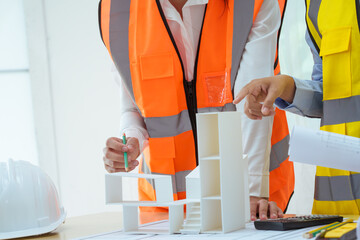 Two young women work at a desk, meticulously designing and drawing plans for building a house. As...