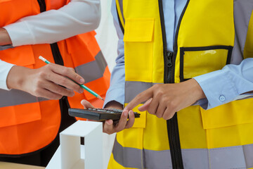 Two young women work at a desk, meticulously designing and drawing plans for building a house. As...