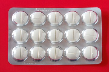 An isolated blister pack containing white pills is prominently displayed against a striking red surface, creating a compelling visual contrast.