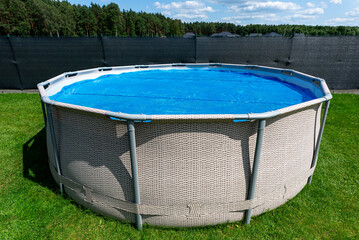 Large expansion pool with a diameter of 3.96 m, located in the yard on the grass, covered with a solar mat.