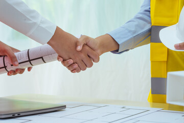 Two young women work at a desk, holding hands while designing and drawing plans for building a...