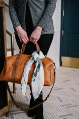 Fototapeta premium Woman holding a brown leather bag with a floral scarf tied to it.