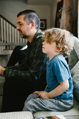 Kid with curly hair sits on couch at home with Dad