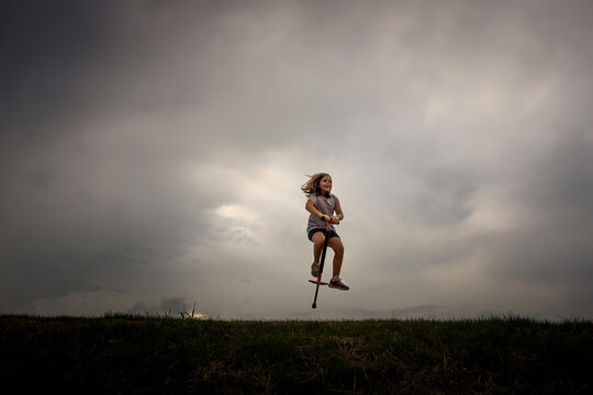 Young girl on pogo stick dramatic sky