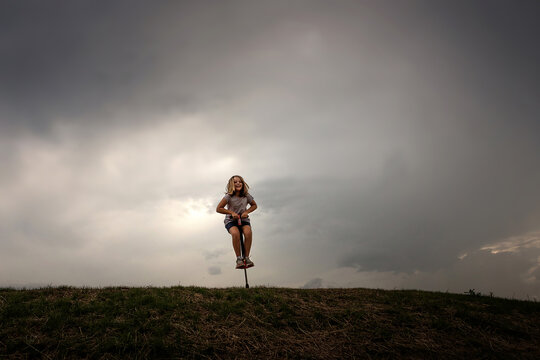 Young girl jumping on pogo stick on top of hill