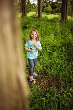 Happy little girl hiding behind tree in forest