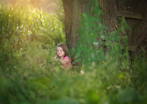 Beautiful young girl sitting against large tree eyes closed