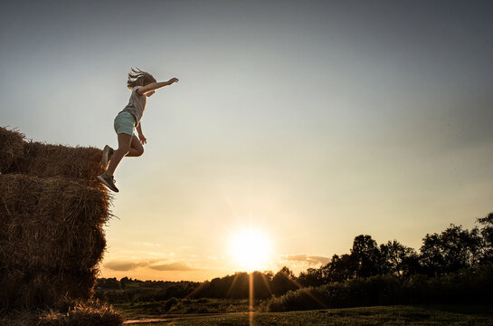 Young girl jumping from straw bales at sunset