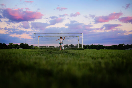 Young girl kicking soccer ball at sunset