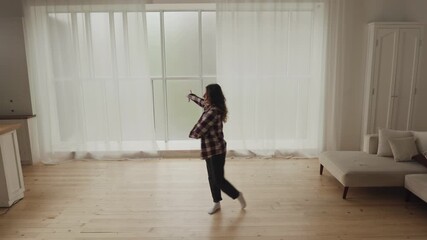 A woman joyfully dances in a sunlit minimalist living room, exuding a carefree and youthful vibe
