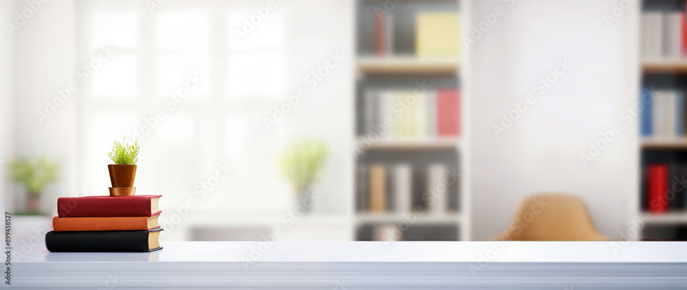 Poster stack of books and a small plant on a white table in a home office with blurred bookshelf background