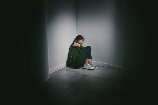 Abuse, alone and scared of woman in dark room, stress and flinching with fear of physical trauma. Mental health, depression or anxiety of female person with sadness, phobia or schizophrenia for girl