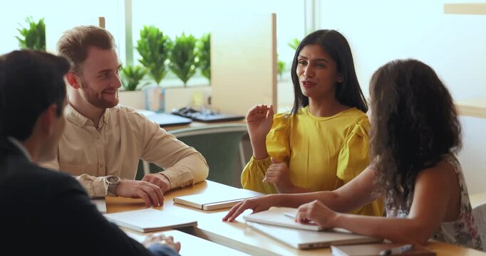 Positive inspired young Indian project manager woman talking to diverse colleagues at meeting, explaining idea for brainstorming. Multiethnic business team in casual discussing teamwork strategy