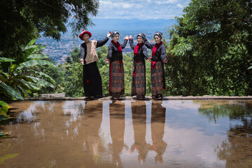 Obraz premium Younger cute Hmong or Yao Hill Tribes teenagers in beautiful traditional dress costumes with flowers in bamboo baskets travel to a natural waterfall in Chiang Mai, Thailand.