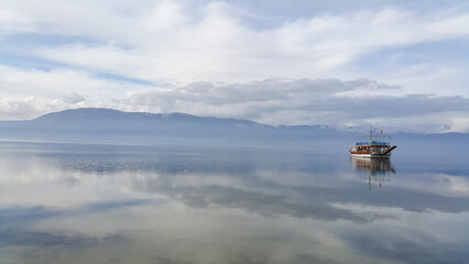 A lonely boat in the middle of the water, snowy mountain ranges on the horizon. Reflection of sky and boat in water