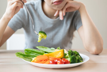 unhappy asian women is on dieting time looking at broccoli on the fork. girl do not want to eat vegetables and dislike taste