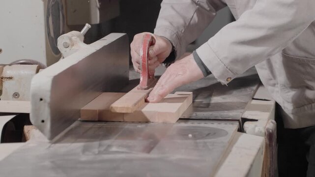A man carpenter processes wooden planks on a benchtop of grinding machine, holds in hands and uses a jointer while working at workbench in a carpentry factory or workshop. Slow motion. Shooting mode