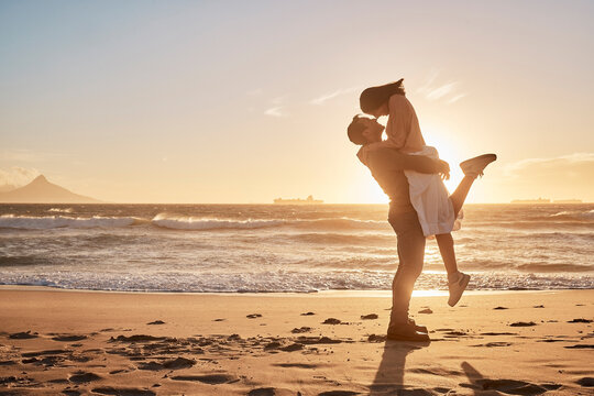 Travel, lifting and couple with sunset at beach for support, relationship or weekend getaway. Love, ocean and happy man hug woman with affection for vacation, anniversary or romantic date in Zanzibar