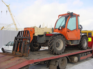 Fototapeta premium Orange forklift on a flatbed truck, ready for transportation at a construction site.