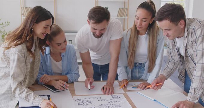 Brainstorming and planning a business teamwork startup. A group of young people at a meeting working on documents at a table in a bright office.A team of students discusses a draft document.