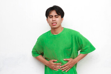 Obraz premium Adult Asian man wearing green shirt posing with gesture of holding body part and showing pain expression on white background.