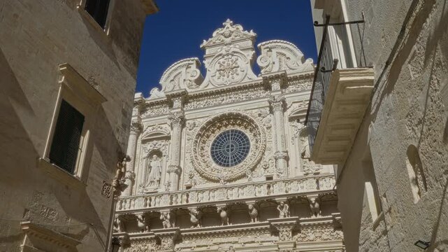 Beautiful intricate facade of the basilica di santa croce against a clear blue sky in lecce, puglia, italy, showcasing impressive architecture, details, window, balcony, and historical charm.