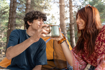 Young couple enjoying coffee while camping in forest, outdoor lifestyle concept