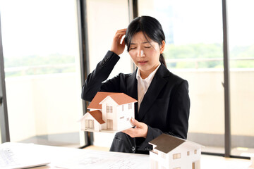 住宅模型を持ちながら悩むビジネスウーマン