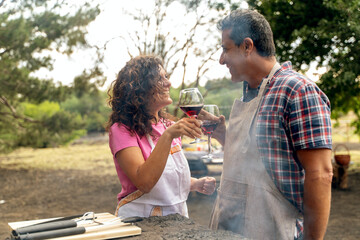 Romantic couple toasting with wine during outdoor barbecue, intimate moment concept