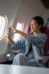 Fototapeta premium Asian traveler women using smartphone to taking photo of sky view through the windows on cabins flight while sitting near windows on business travel class flight in airplane with vacation lifestyle