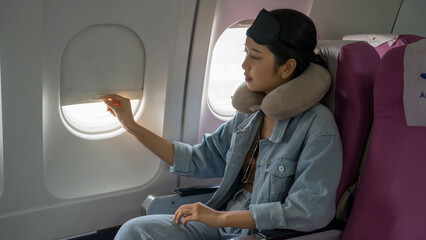 Asian traveler women pulling down to closing window in cabin flight and prepare to taking sleep on plane flight while sitting near windows on business travel class in airplane with vacation lifestyle