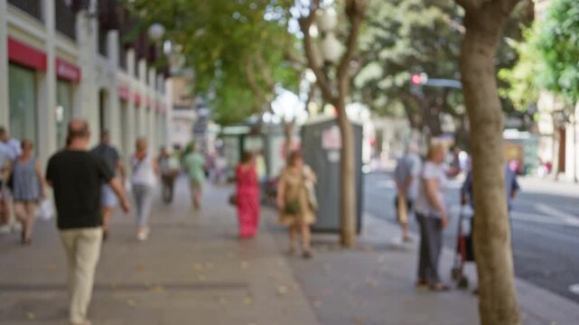People walking outside on a sunny urban street with blurred trees in the background showing an outdoor city environment