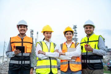 Group of Asian engineer people with safety helmet standing front of oil refinery. Industry zone gas petrochemical. Factory oil storage tank and pipeline. Workers team work in refinery construction