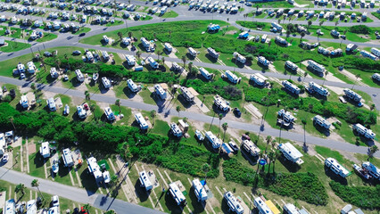 Large RV park campsite long row of recreational vehicles trailers boats tall palm trees in South Padre Island beach Gulf Coast shoreline, aerial view campers basecamp with power hookup, Texas