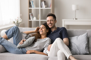 Obraz premium Cheerful wife and husband relax on cozy sofa in modern living room, have fun laughing and joking, enjoy leisure time together, feel love, closeness, share funny memories, relish pleasant conversation