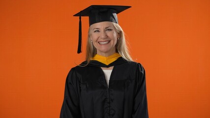 Portrait of happy senior graduate student woman in mortar board with diploma laughing over orange...