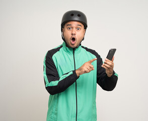 Young asian rider wearing green jacket uniform and bike helmet standing holding smartphone food application on isolated. Male delivery service worker. Delivery courier and shipping food service.