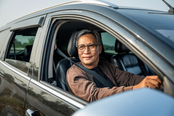 Senior Asian man drives a car vehicle on a clear day. With beautiful blue sky. He smiling driving to travel by car. Old man getting new car.