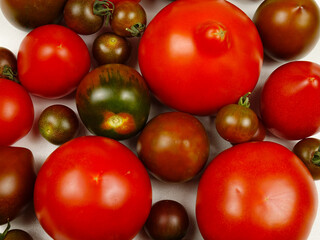 Fresh red and brown tomatoes of different varieties placed on a white table, background