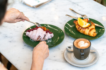 Top of senior woman eating croissant blueberry with hot coffee on dessert table at cafe.