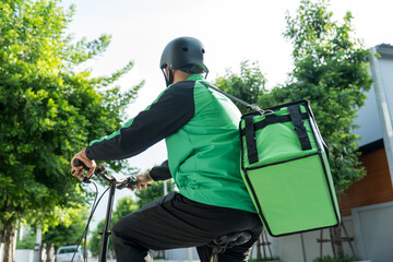 Portrait Rider food delivery man wearing green uniform and helmet cycling a bicycle the food service to customer. Happy delivery man with green backpack shipping of goods to customers.