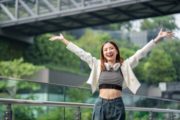 Young asian woman fashion lifestyle with headphone standing posing in urban city downtown. Happy...