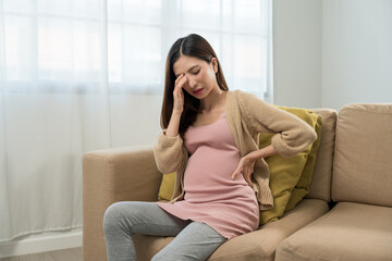 Young pregnant woman suffering from headache and abdominal pain alone at home, tired and stressed female during pregnancy, accidental medical urgency case and health care insurance for pregnancy.