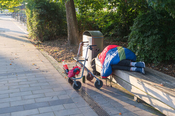 Ein Obdachloser schläft auf einer Parkbank , davor sein Rollator
