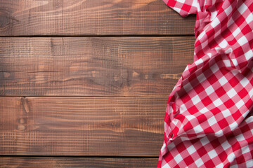 Red and white checkered tablecloth on rustic wooden table, perfect for picnic, food backgrounds, or country-themed decor.