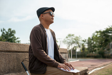 Young blind man sitting outside read some braille text on page paper Finger of blind student...