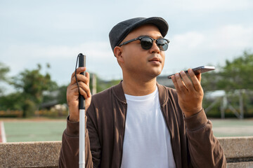 Young asian blind man using application on mobile phone to helping accessibility for persons with...