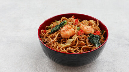Mie Goreng Udang or Bakmi Goreng Sea Food or Fried Noodle with Sea Food. Indonesian food and cuisine, Adopted from Chinese cuisine. served on black red bowl isolated on grey