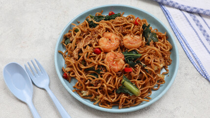 Mie Goreng Udang or Bakmi Goreng Sea Food or Fried Noodle with Sea Food. Indonesian food and cuisine, Adopted from Chinese cuisine. served on blue plate isolated on grey