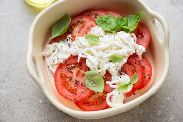 Beige serving tray with sliced tomatoes, stracciatella or stretched curd cheese and basil, horizontal shot, middle close-up, selective focus